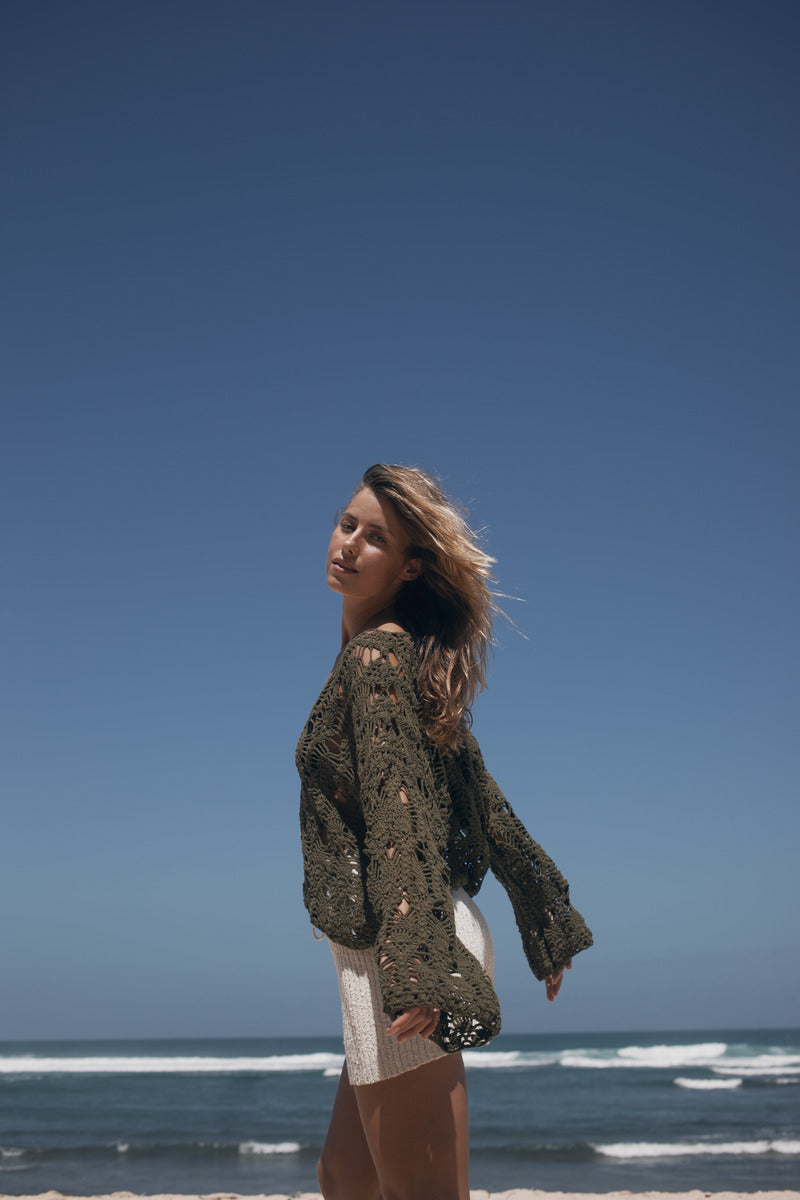 Woman standing on a beach with clear blue sky and ocean waves.