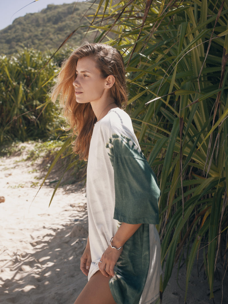 Woman in a white and green dress standing on a sandy path with plants around