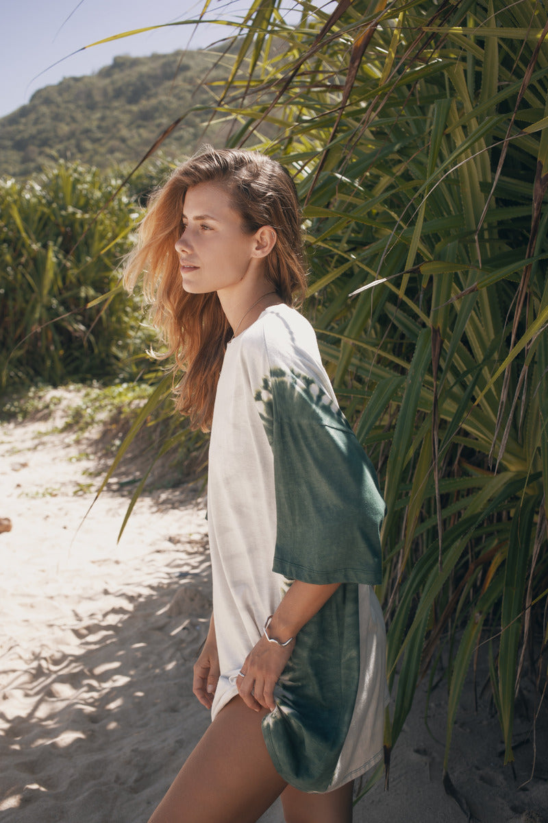 Woman in a white and green dress standing on a sandy path with plants around
