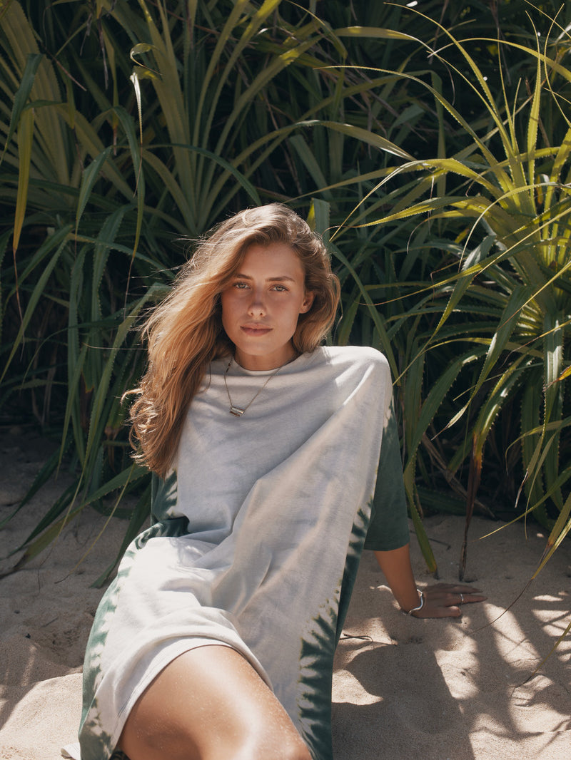 Woman sitting on sand with greenery in the background