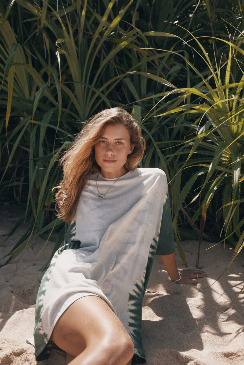 Woman sitting on sand with greenery in the background