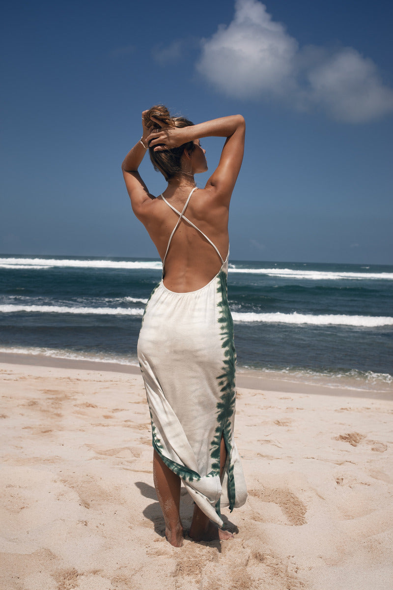 Model in a white cototn hemp tie dye dress standing on a beach with ocean waves in the background