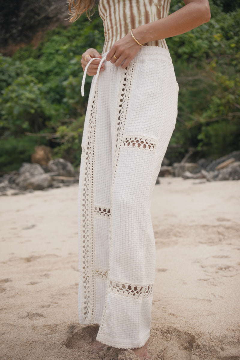 Womens striped tie dye bodysuit and white crochet pants on a beach.