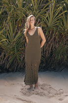 Woman wearing a green crochet dress standing on a sandy beach with palm trees in the background