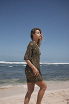 Woman in a green dress standing on a beach with clear blue sky and ocean.