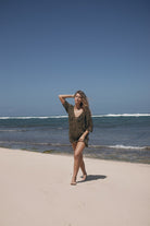 Woman standing on a sandy beach with ocean waves and clear blue sky.