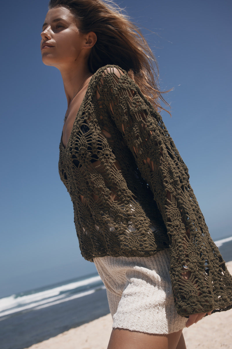 Woman wearing a crochet cardigan on a beach with clear blue sky