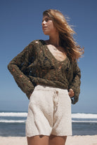 Woman wearing a green crochet sweater and beige shorts standing on a beach.