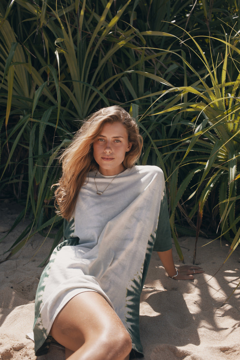 Woman sitting on sand with greenery in the background