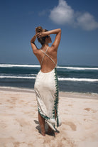Model in a white cototn hemp tie dye dress standing on a beach with ocean waves in the background