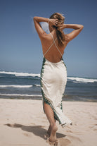 Woman in a white and green dress walking on a beach with waves in the background