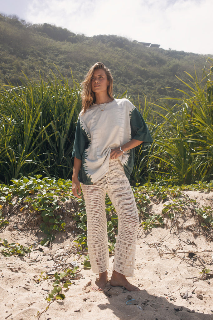 Woman standing on a sandy path with greenery and mountains in the background