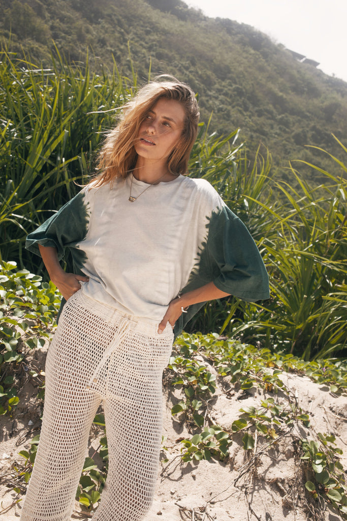Woman standing in a natural setting with greenery and mountains in the background