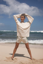 Woman in a white outfit standing on a beach with ocean waves in the background