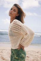 Woman wearing a beige crochet top on a beach with ocean and sky in the background