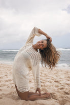 Woman in a white crochet dress on a beach with ocean and sky in the background
