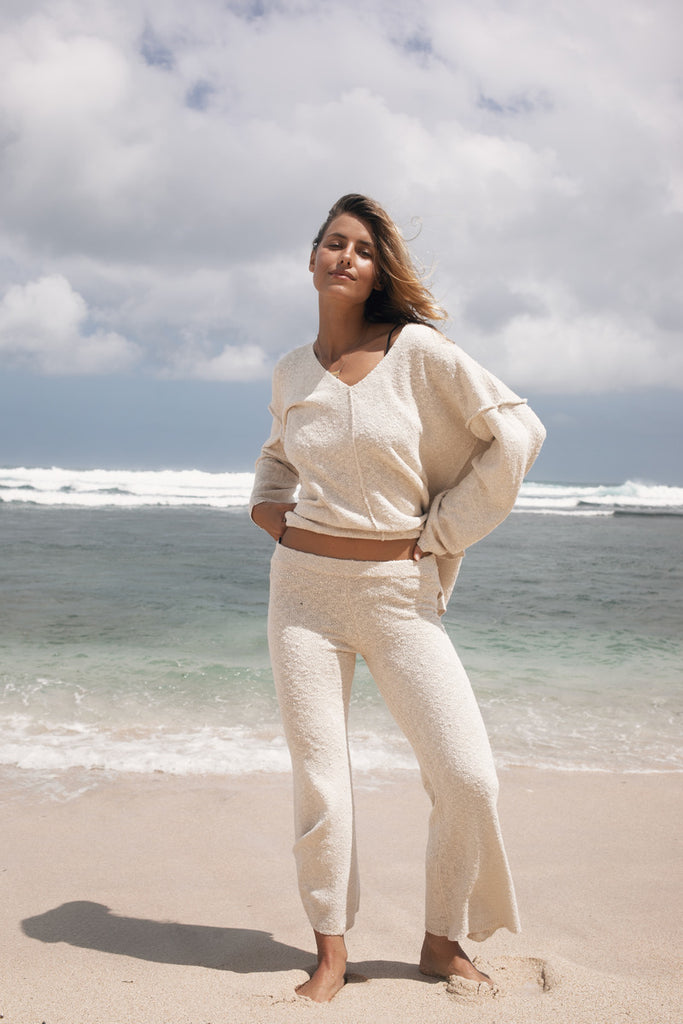Woman in a beige outfit standing on a beach with ocean waves in the background