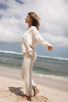Woman in a beige textures set standing on a beach with ocean waves in the background