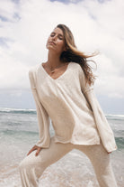 Woman in a beige outfit standing on a beach with ocean and sky in the background