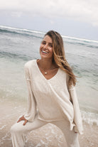 Woman in a white outfit sitting on a beach with ocean waves in the background