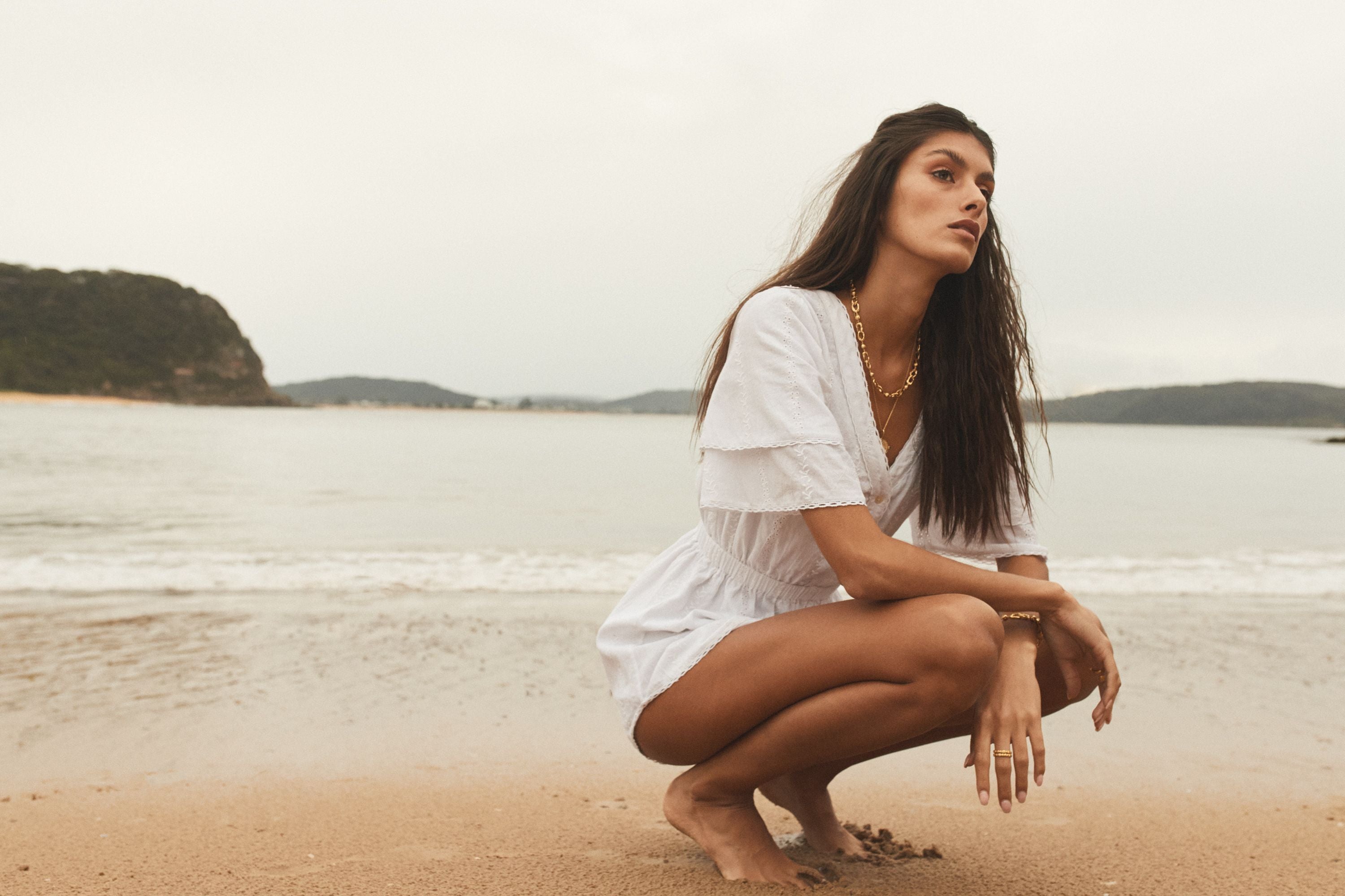 girl crouching on beach in white mini dress